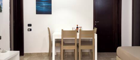 A room with a white table and two chairs, a beige sofa, a dark wooden door, and a framed picture on the wall.