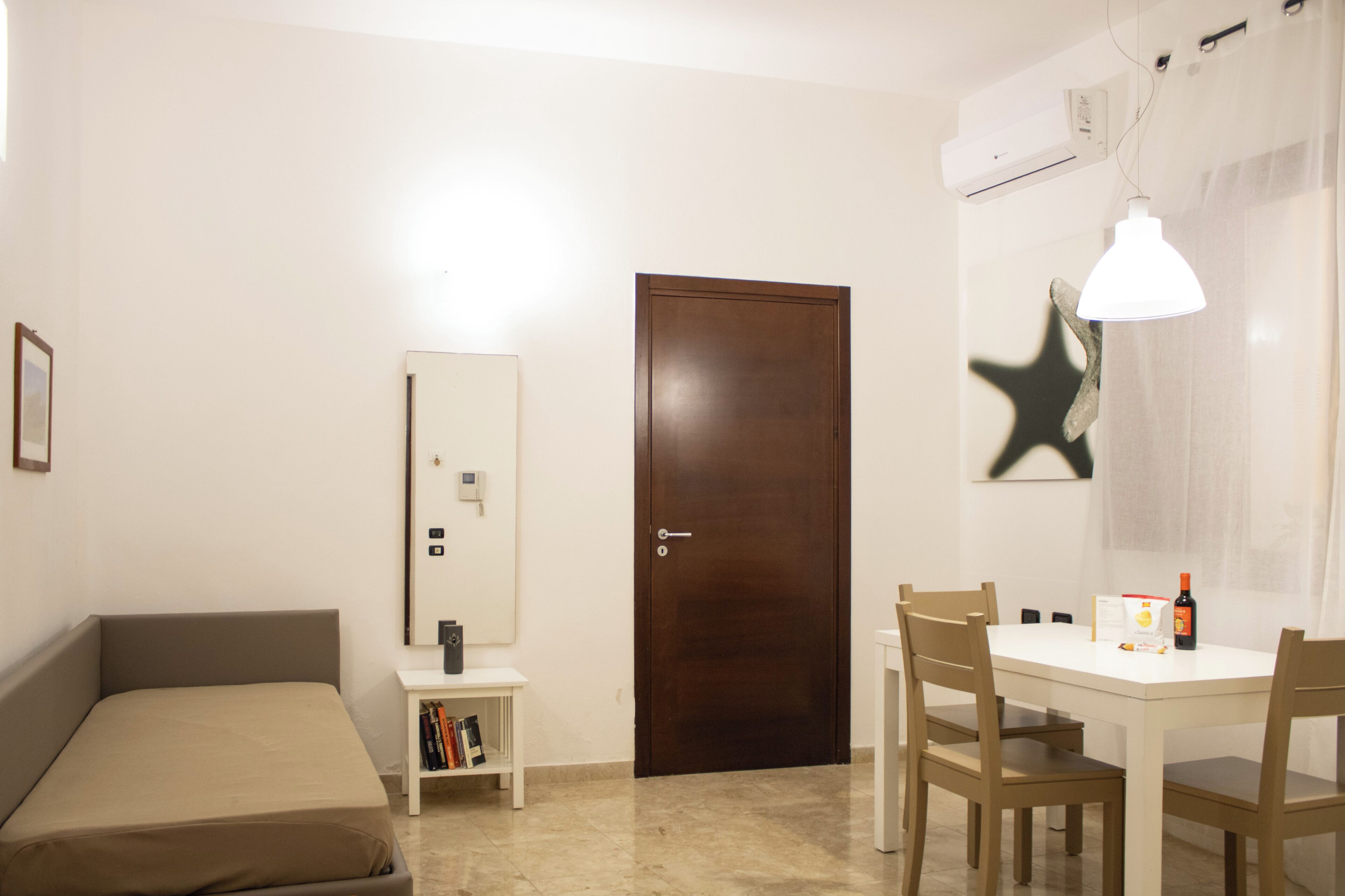 Una habitación con cama, escritorio, sillas, una puerta y un equipo de aire acondicionado.