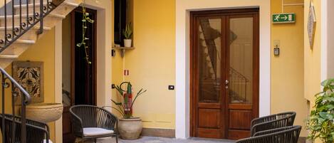 A courtyard with wicker chairs, a potted plant, and a wooden door.
