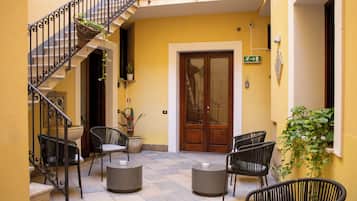Un patio con escaleras, sillas de mimbre, una puerta de madera y plantas en macetas.