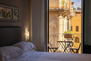 Ein Hotelzimmer mit Bett, Nachttisch, Wandlampe und Blick auf einen Balkon mit Tisch und Stühlen.