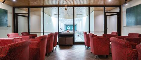 Un salón de conferencias con sillas de diseño rojo, techo de madera y ventanas amplias.