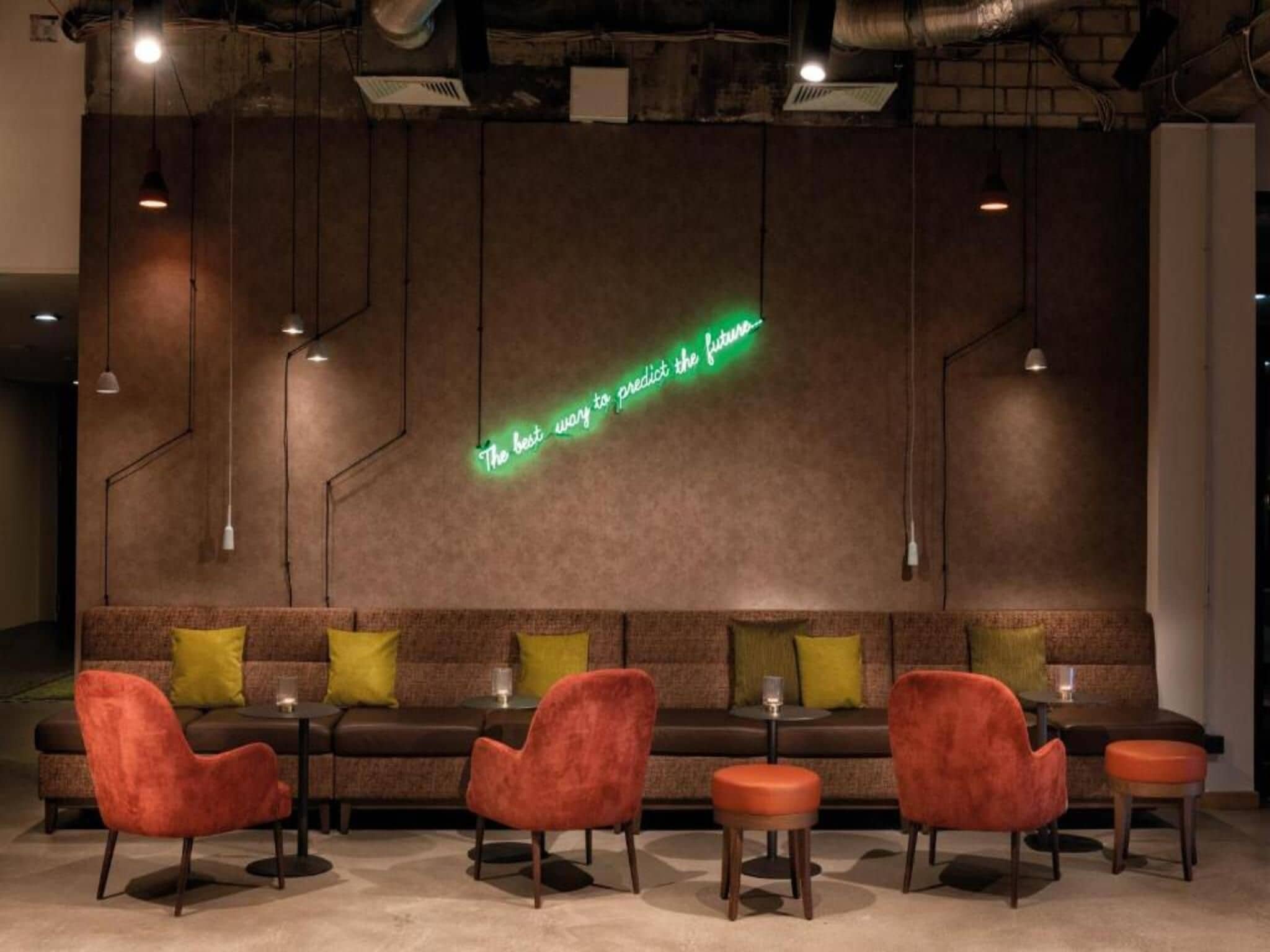 A modern lounge area with a neon sign, sofas, and red chairs.