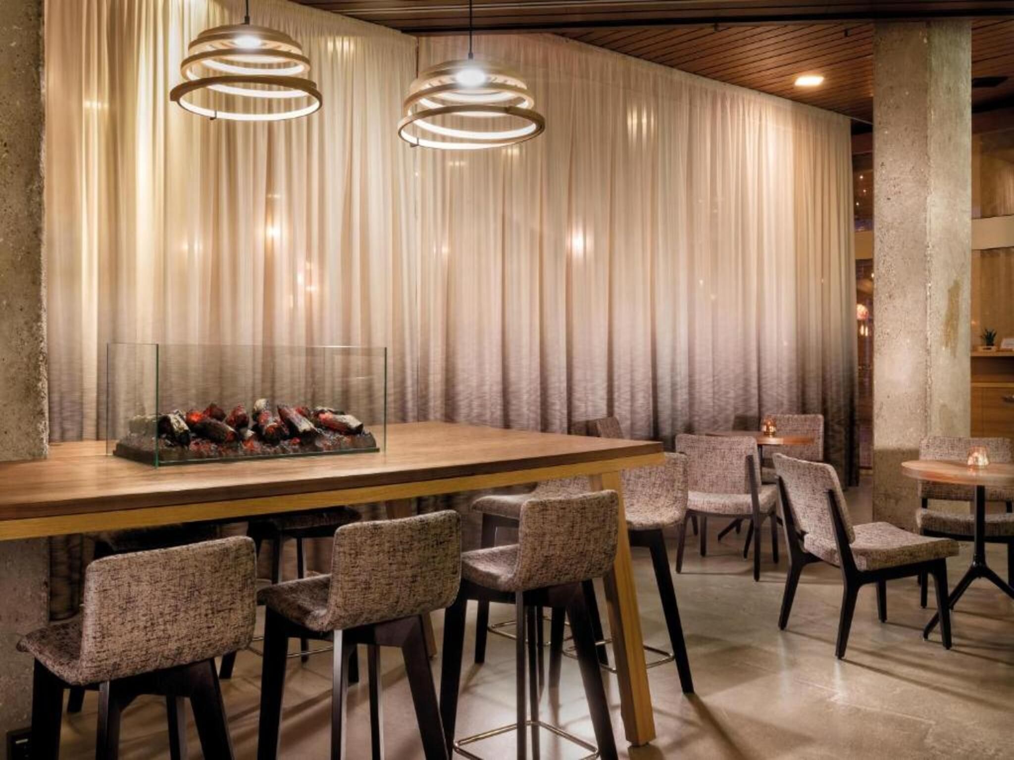 Ein Restaurantinneres mit einer langen Holztheke, mehreren gepolsterten Stühlen und Pendelleuchten.