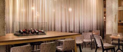 A restaurant interior with a long wooden bar, multiple upholstered chairs, and pendant lighting.
