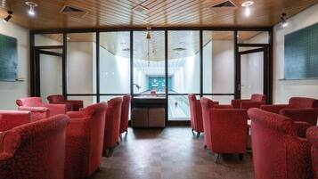A room with red upholstered chairs arranged in rows, large windows, and a wooden ceiling.