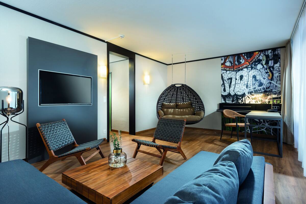 A modern living room with a flat-screen TV, two chairs, a coffee table, and a sofa.
