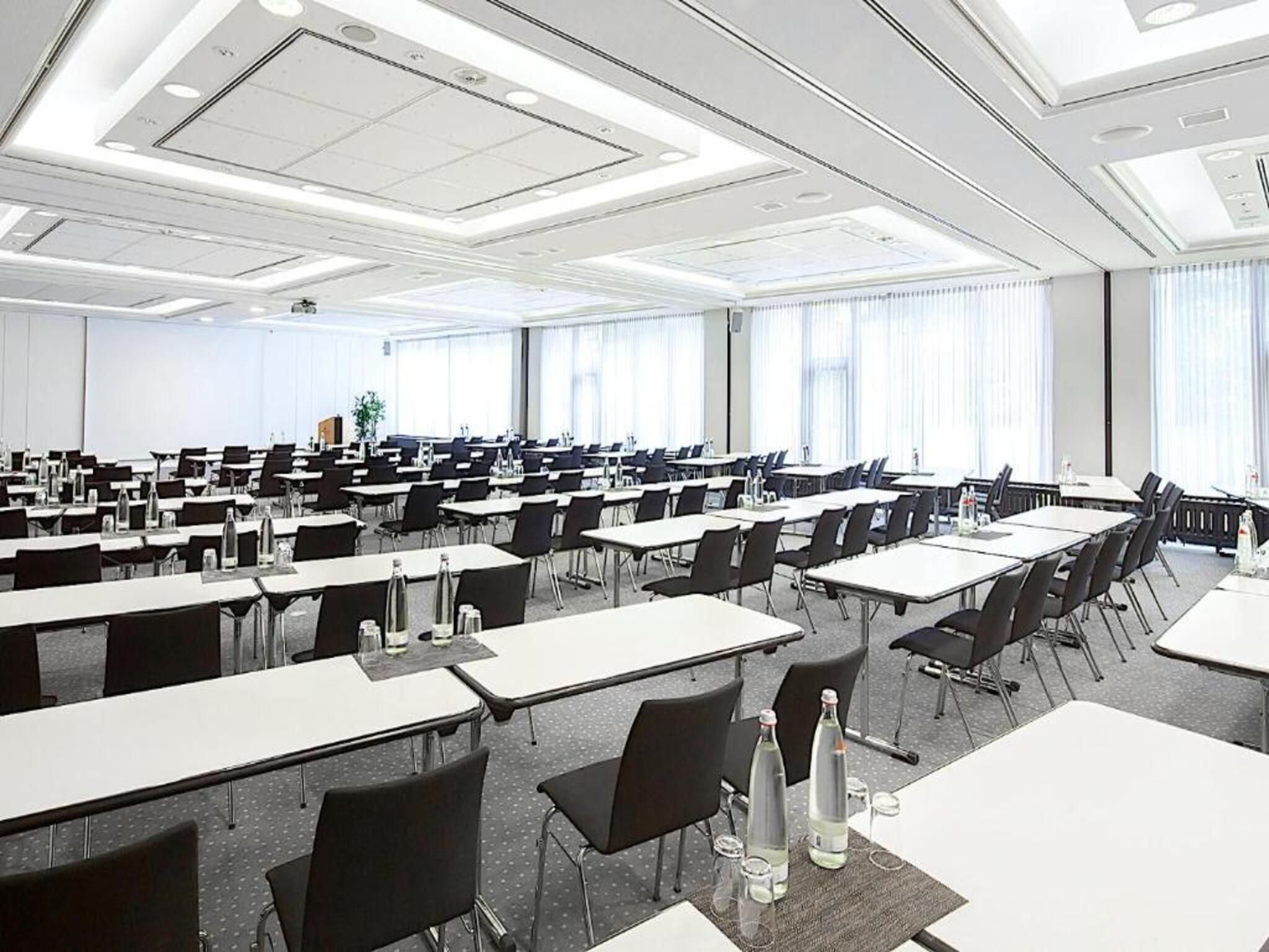 Un amplio salón de conferencias con varias mesas y sillas dispuestas en filas.