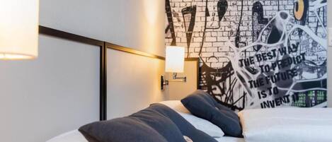 A modern hotel room with a bed, pillows, a wall with graffiti art, and a nightstand with a lamp.