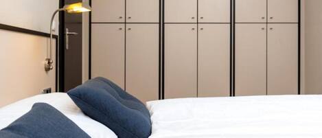 Un dormitorio con cama, almohadas, mesita de noche y armario.