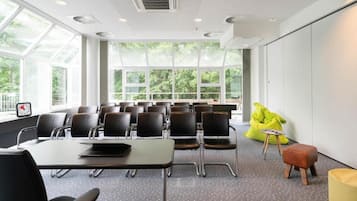 Un salón de conferencias con una amplia mesa, varias sillas, un proyector y vistas a la vegetación a través de grandes ventanales.