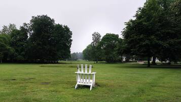 A white Adirondack chair in a grassy field with trees in the background.