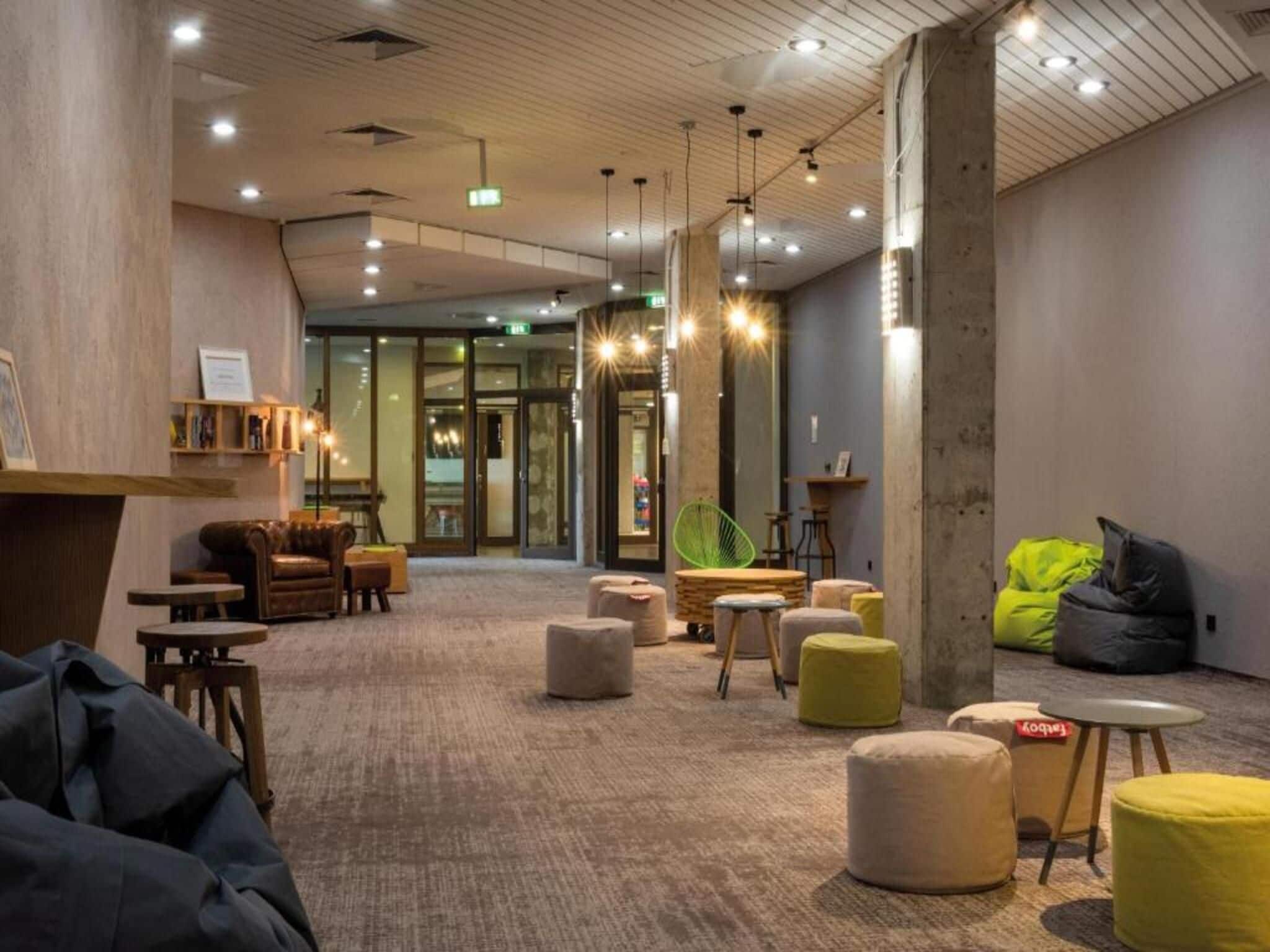 Een moderne lounge met zitplaatsen, tafels en een zichtbare nooduitgang.