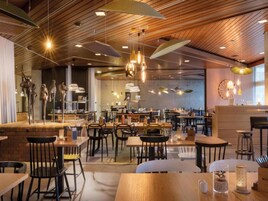 Un restaurante espacioso con vigas de madera en el techo, lámparas colgantes y diversas opciones de asientos, incluyendo mesas y sillas.