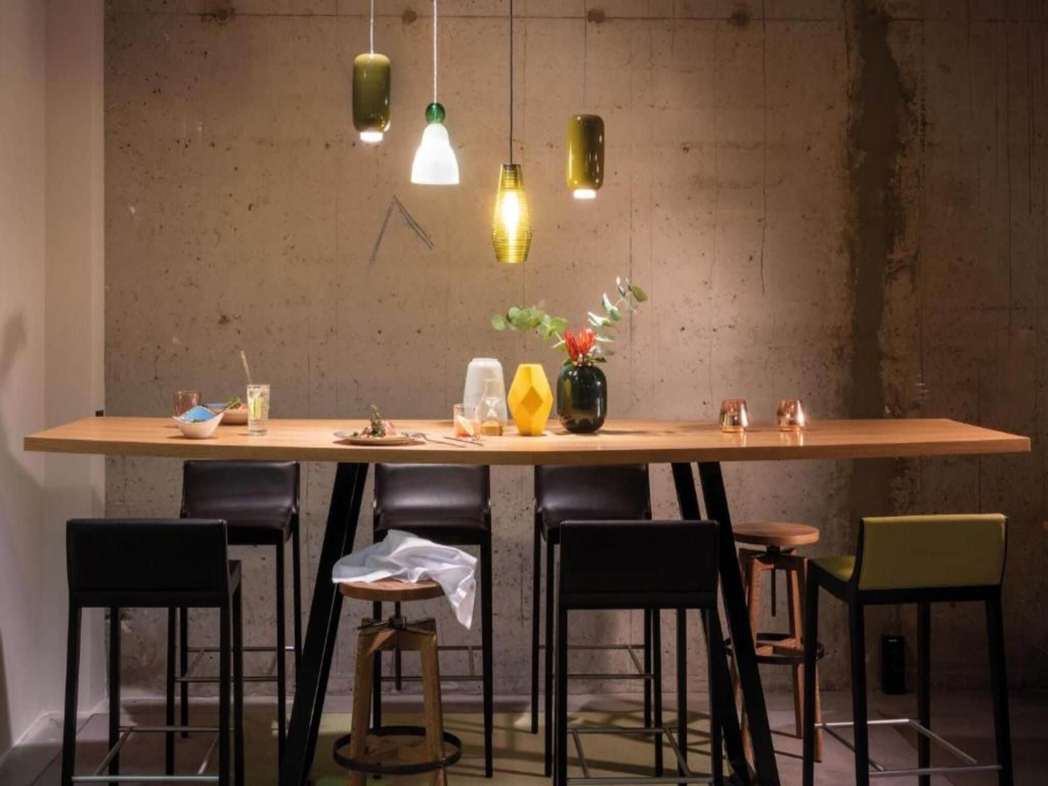 A dining area with a long table, six chairs, and hanging pendant lights.