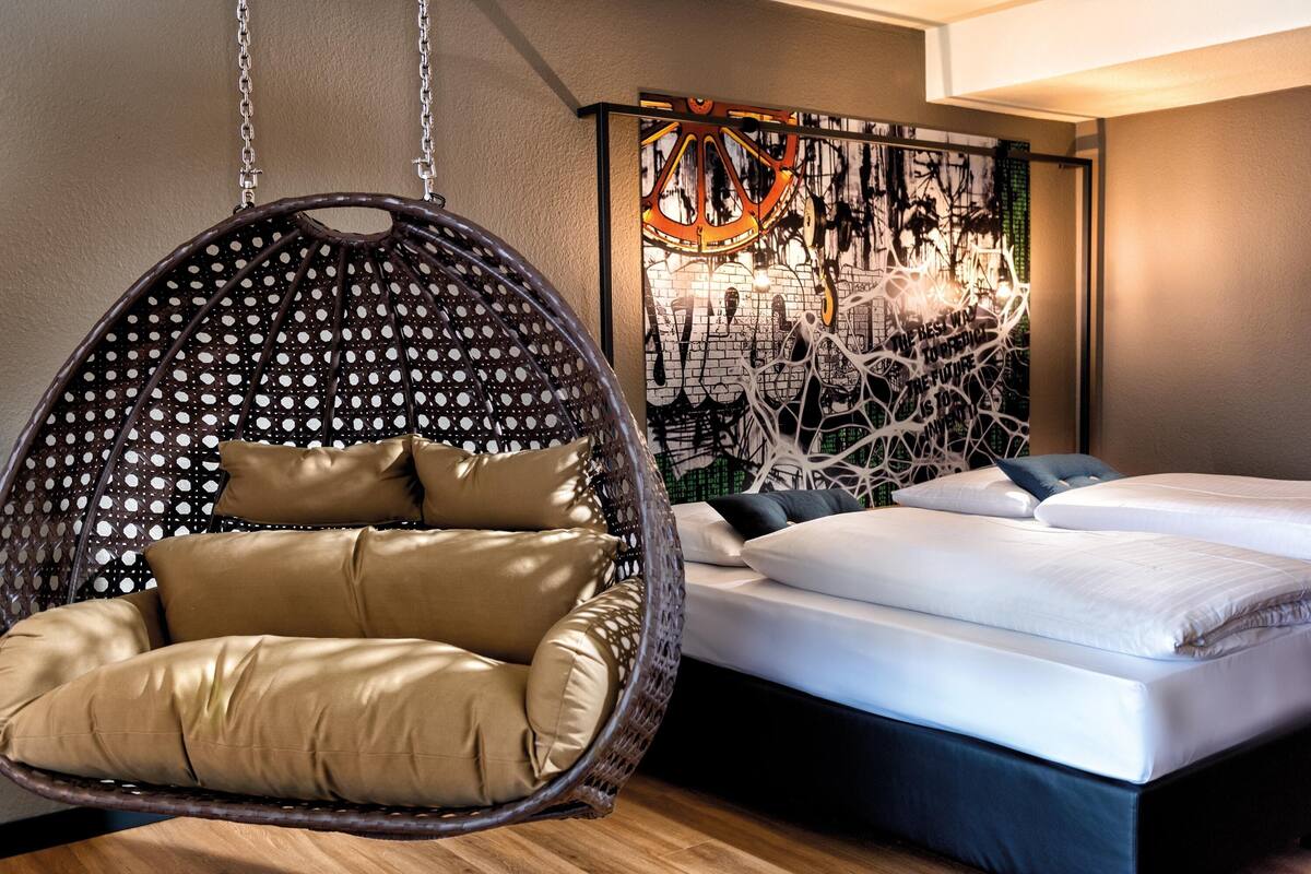 A modern bedroom with a hanging chair, a bed with white linens, and a wall art piece.