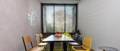 A room with a table, chairs, a rug, and a window with blinds.