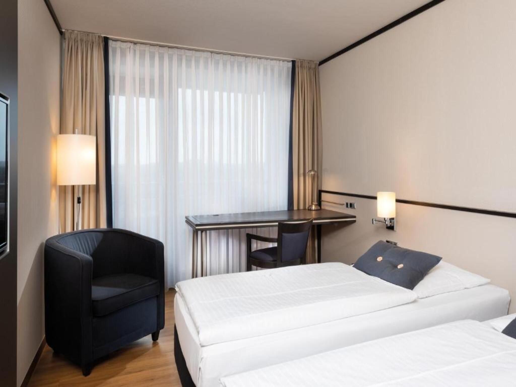 Et hotelværelse med to senge, et skrivebord, en stol og et fjernsyn.