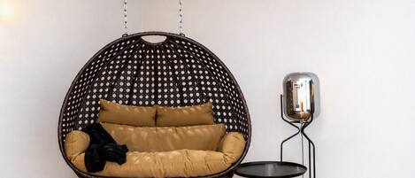 Une pièce avec un fauteuil suspendu, une petite table et une lampe fixée au mur.