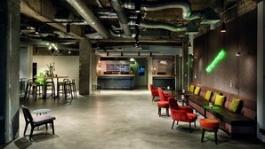 Un vaste espace intérieur comprenant un long canapé rouge, une table en bois avec des chaises et un néon vert fixé au mur.