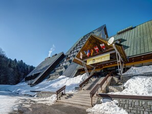 Un bâtiment moderne doté d’un toit en pente et de nombreuses fenêtres. Un escalier mène à l’entrée, et on peut voir un panneau orné de drapeaux.