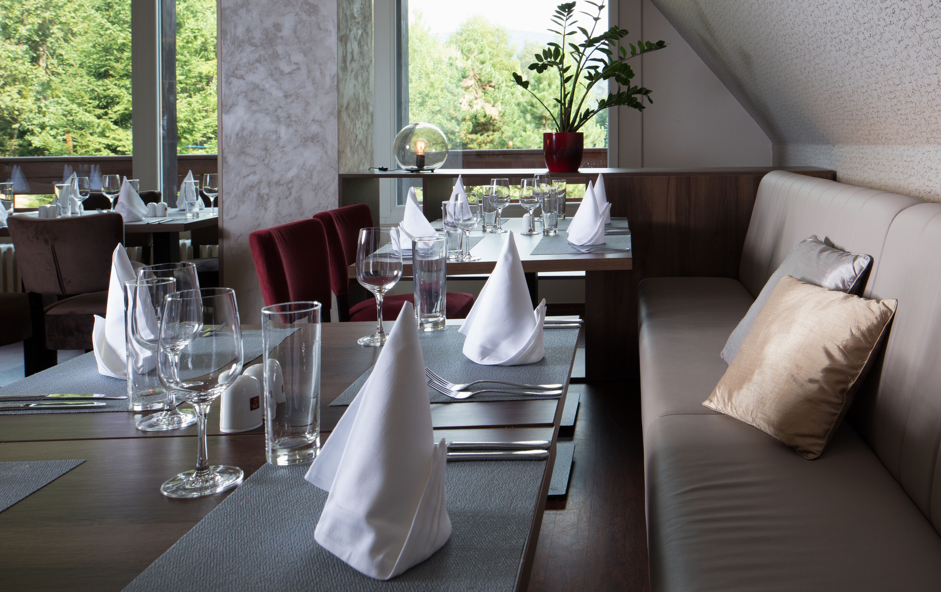 A restaurant with tables set for dining, a sofa with cushions, and a potted plant on a shelf.