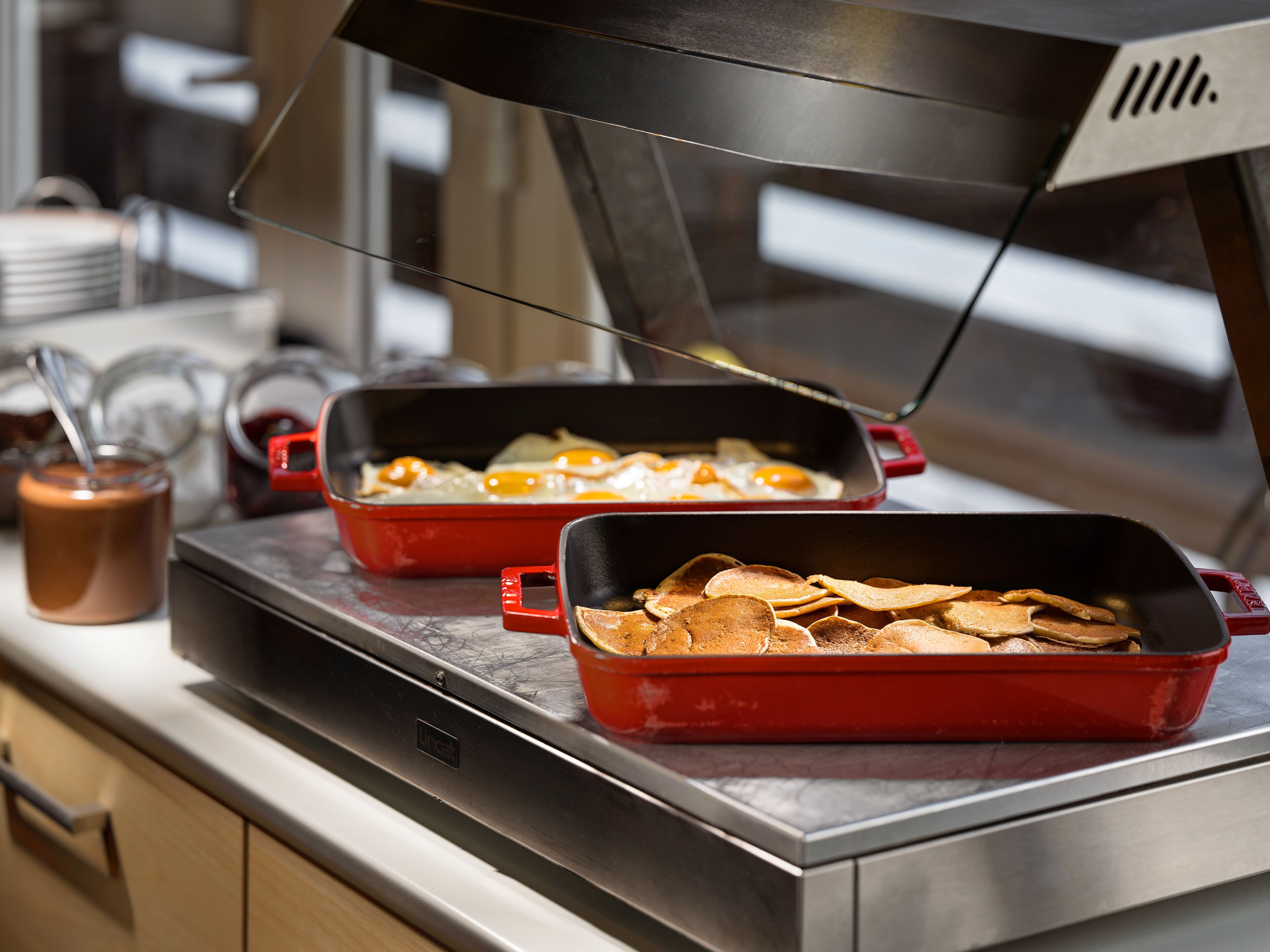 A kitchen counter with two red baking dishes, one containing eggs and the other with pancakes.