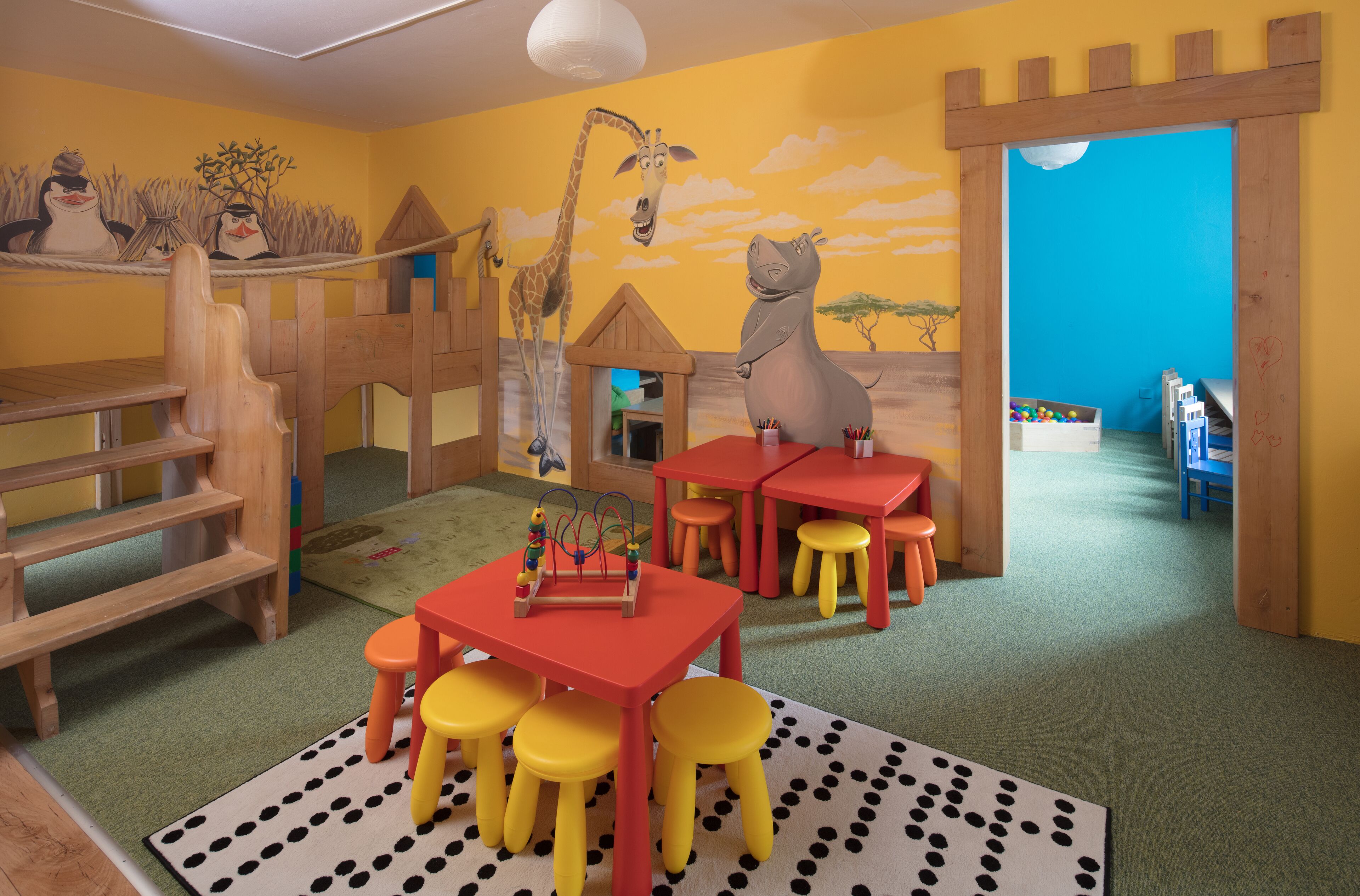 Ein Spielzimmer für Kinder mit Holzspielgeräten, einem Tisch mit Stühlen und einer Wandmalerei.