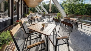 An outdoor patio with tables and chairs, large windows, and a view of trees and mountains. - Pinia Hotel & Resort (Spindleruv Mlyn)