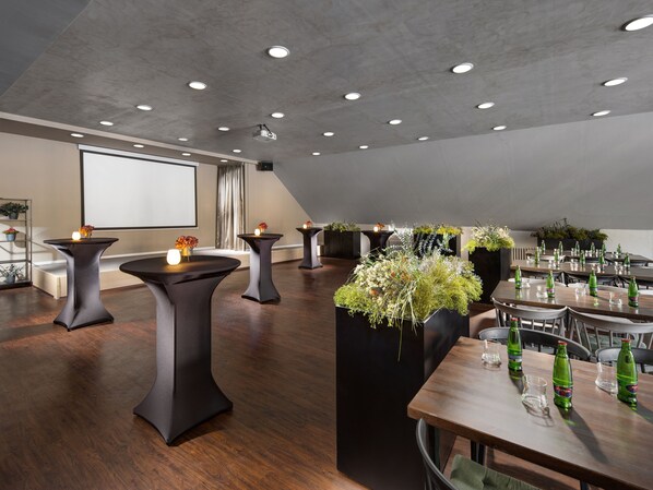Une salle de conférence moderne équipée de tables rondes, d’un projecteur et d’un grand écran.