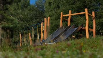 A playground with a slide and climbing structures in a grassy area with trees in the background.