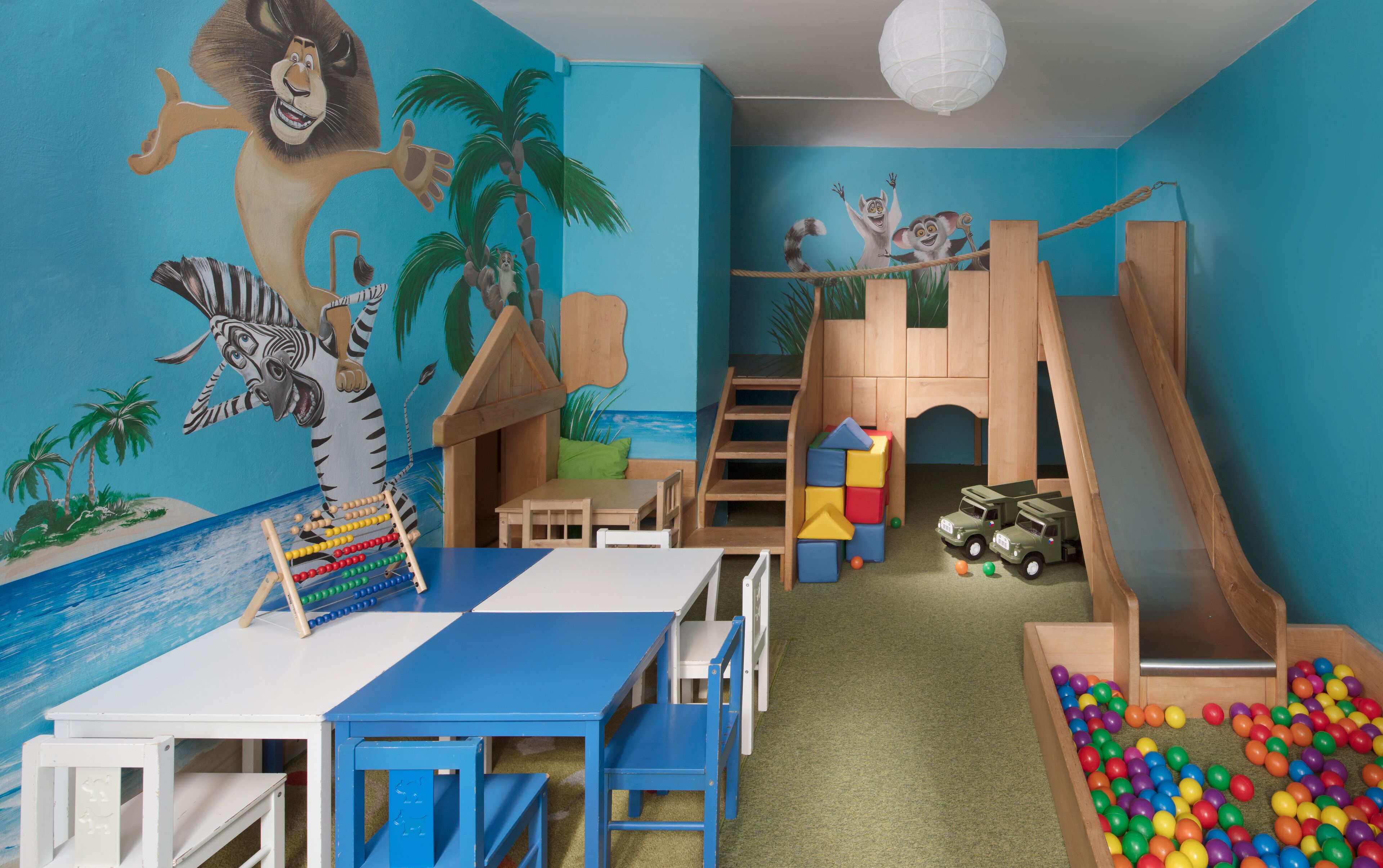 A playroom with a slide, climbing wall, and a beach-themed mural.
