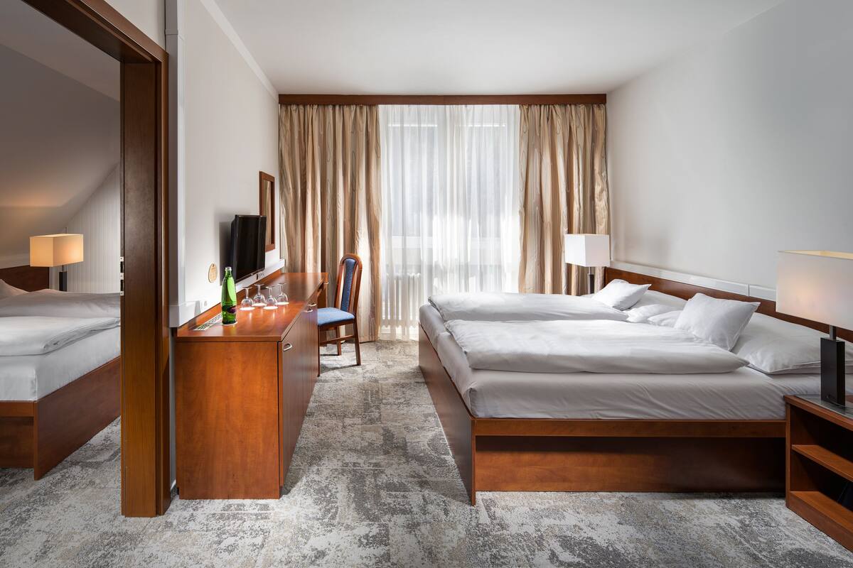 Ein Hotelzimmer mit zwei Betten, einem Schreibtisch mit Fernseher und einem großen Fenster mit Vorhängen.