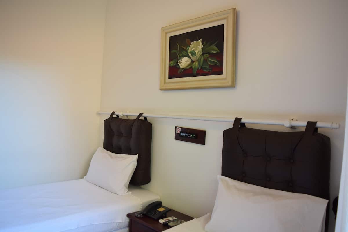 Une chambre d’hôtel avec deux lits, une table de chevet avec un téléphone et une télécommande, un tableau au mur et un panneau indiquant qu’il est interdit de fumer.