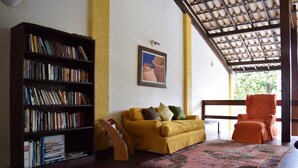 Uma sala de estar com estante, um sofá amarelo, uma poltrona laranja e um tapete estampado.