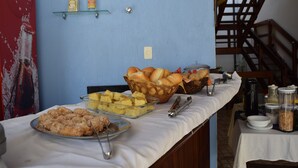 Mesa de buffet com diversos alimentos, um cartaz de Coca-Cola e uma escadaria ao fundo.