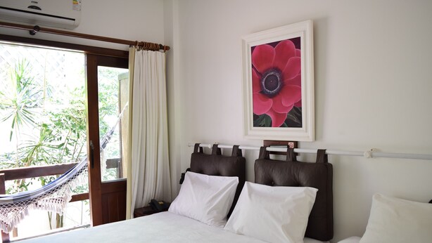 Quarto de hotel com cama, rede e vista para o verde lá fora.