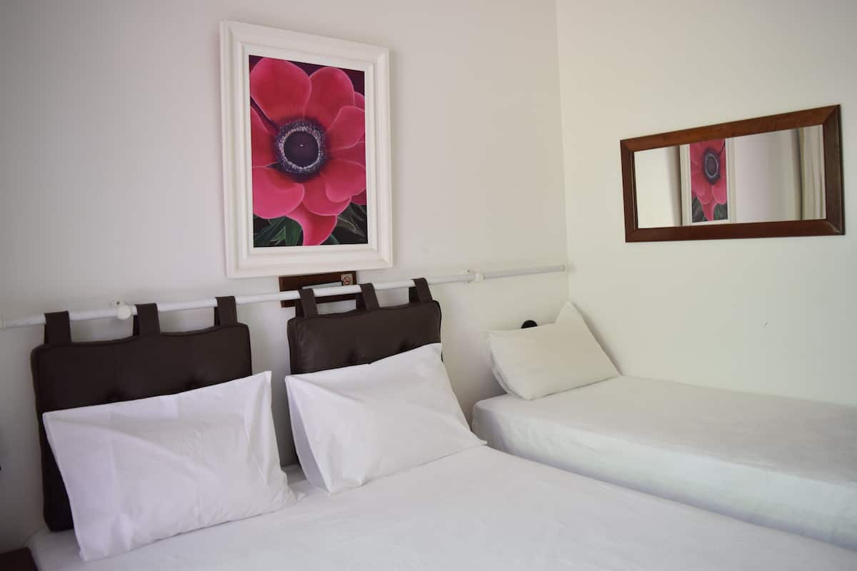 Un lit double avec du linge de lit blanc, une tête de lit et une œuvre d’art florale encadrée au-dessus.