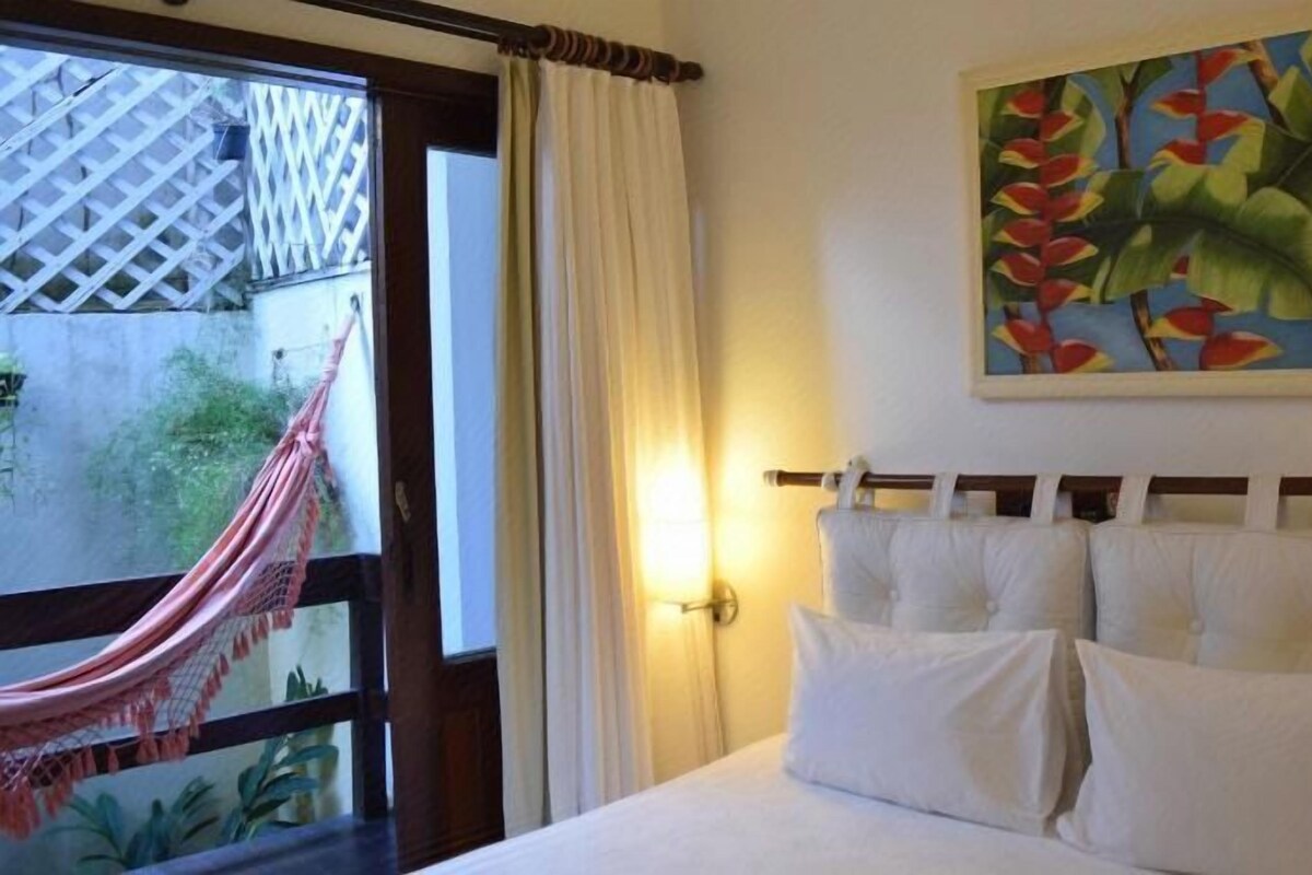 Une chambre d’hôtel avec un lit, une fenêtre donnant sur un paysage verdoyant et un hamac à l’extérieur.