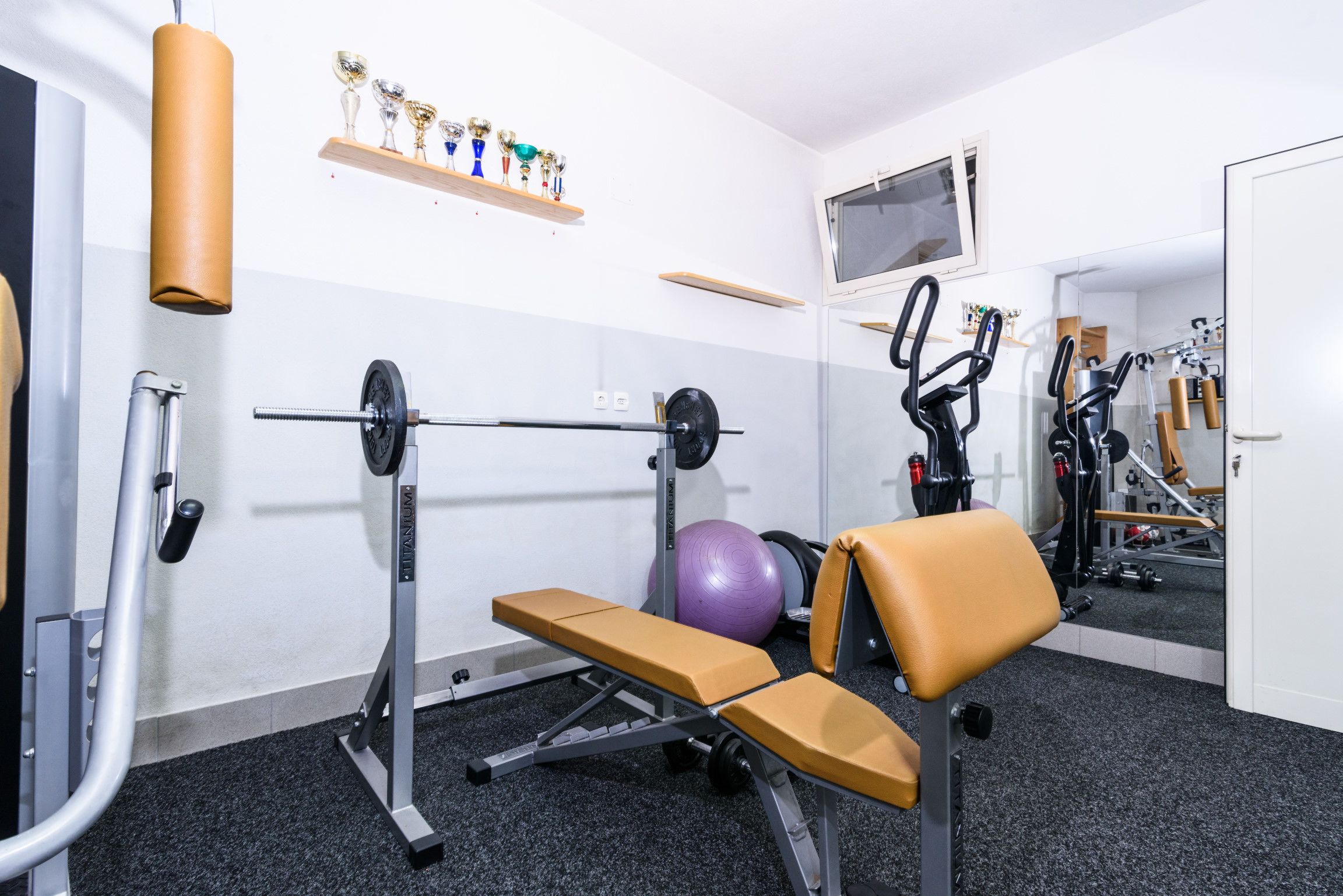A gym with a bench, weight bench, exercise ball, and various fitness equipment.