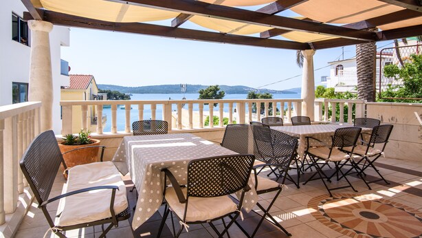 An outdoor patio with tables and chairs, a view of the sea, and a building in the background. - Villa Lavandula (Trogir)