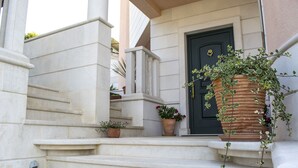 A set of stone steps leading to a black door with a gold handle, flanked by potted plants and a large terracotta pot with climbing plants. - Villa Lavandula (Trogir)