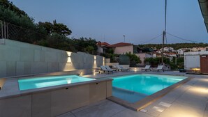 A swimming pool with lounge chairs and a stone wall. - Villa Lavandula (Trogir)