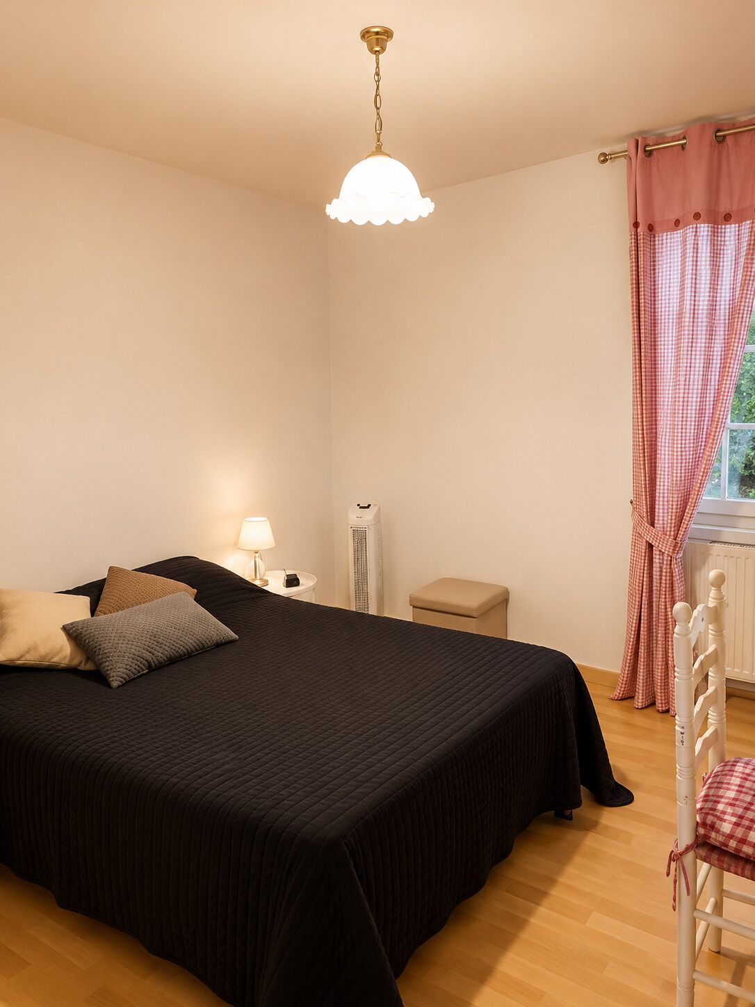 A bedroom with a bed, bedside table, lamp, air conditioning unit, and a window with curtains.