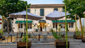 An outdoor seating area with tables and chairs, umbrellas, and a building with a restaurant sign. - Auberge La Crémaillère (Villandraut)