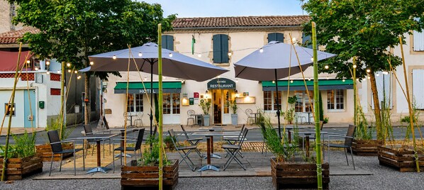 Un espacio al aire libre con mesas, sillas, sombrillas y un edificio con un letrero de restaurante.