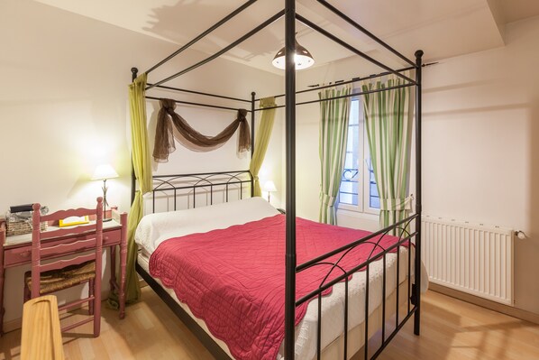 Una cama con dosel con un edredón rojo, un escritorio de madera con una silla y un radiador.