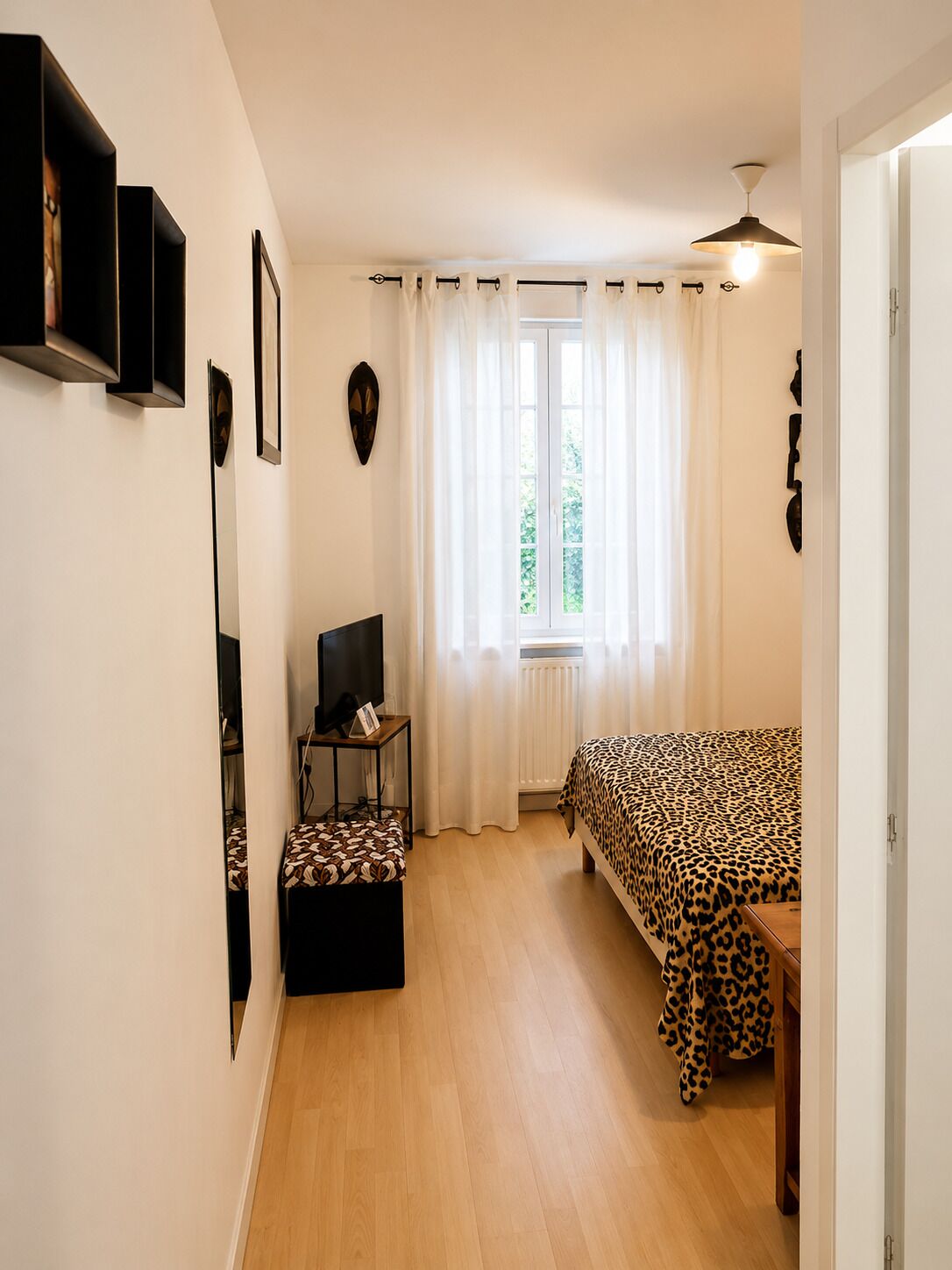 A room with a bed, a television, a small table, and a window with curtains.
