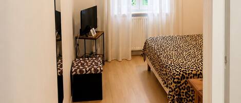 A room with a bed, a television, a small table, and a window with curtains.