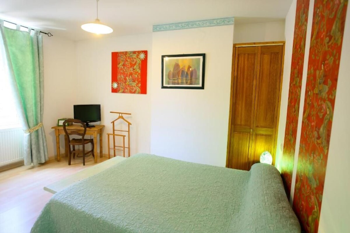 Un dormitorio con cama, escritorio con computadora, silla, armario y dos cuadros en la pared.